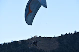 Adventurous travelers paragliding over the rolling hills of Bir Billing on a clear day.