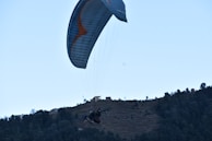 A paraglider soaring above the emerald hills and coastline, capturing the thrill of flying.