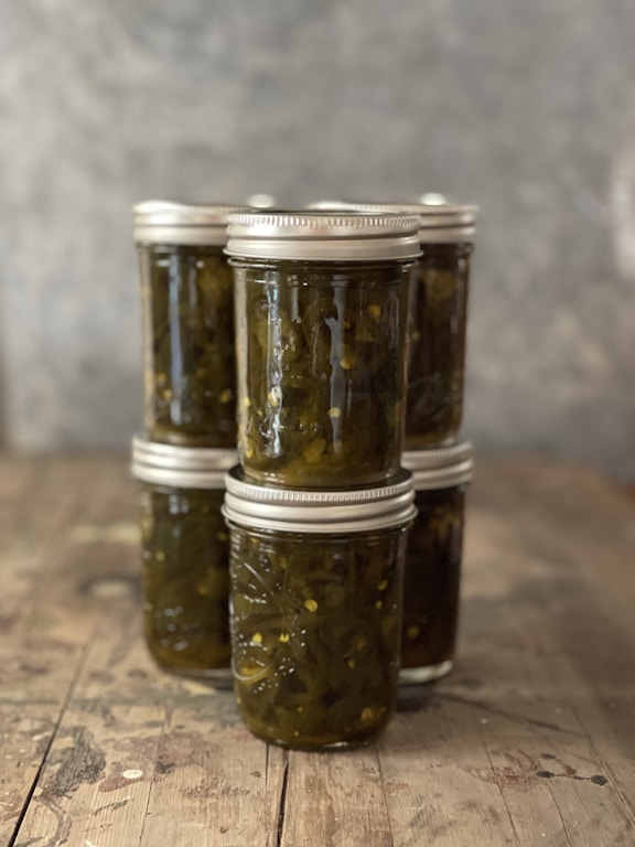 Four jars of colorful refrigerator pickles sitting on a wooden table