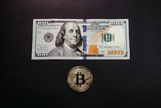 a $ 100 bill and a bitcoin on a table
