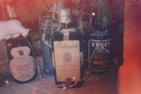 Several bottles of cherry brandy and other alcoholic beverages are arranged on a surface. Decorated tree branches are partially visible, suggesting a festive context. Soft lighting creates a warm and cozy ambiance.