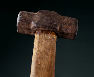 Close-up of a craftsman’s hands gripping a well-worn hammer over a wooden workbench.