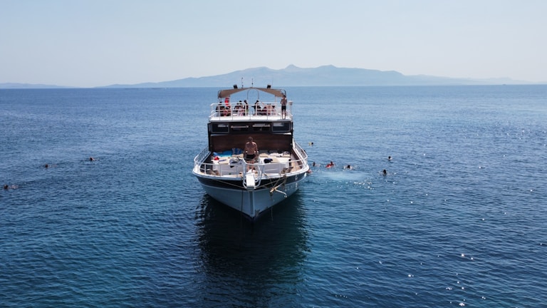 Guests taking a swimming break in the clear blue sea with the pirate ship anchored nearby under cinematic lighting