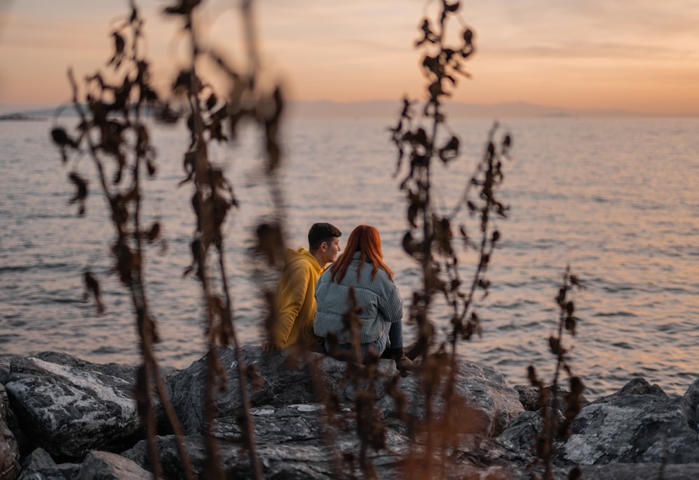 two people sitting on a rock near the water