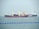 Two large cargo ships are navigating through the water. The ship closer to the viewer has a prominent red hull and yellow cranes, while the ship in the background has the word 'TANKER' visible on its side. The sea is calm with a series of blue buoys in the foreground.