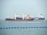 Two large cargo ships are navigating through the water. The ship closer to the viewer has a prominent red hull and yellow cranes, while the ship in the background has the word 'TANKER' visible on its side. The sea is calm with a series of blue buoys in the foreground.
