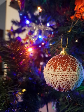 A close-up of a Christmas tree adorned with colorful ornaments and an OrbitBuddies tumbler resting beneath it, glowing softly in warm lights.