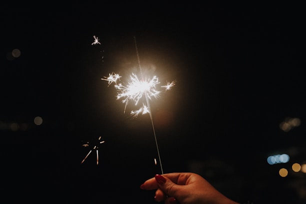 A close-up of hands carefully lighting a firework fuse amid glowing sparks and smoke.