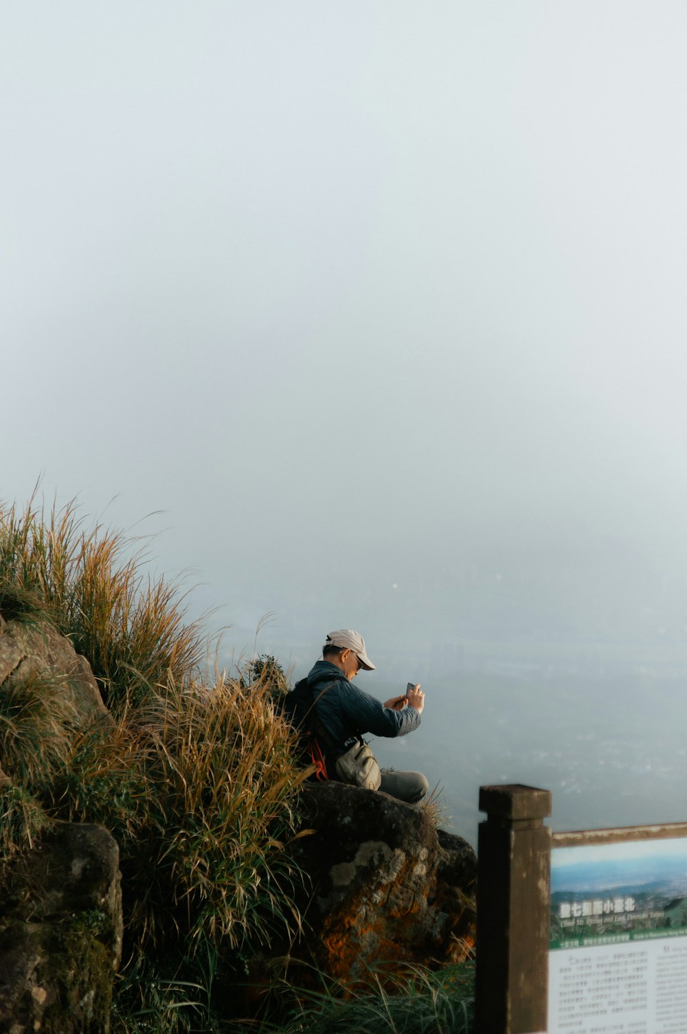Un uomo seduto sulla cima di una montagna accanto a un cartello