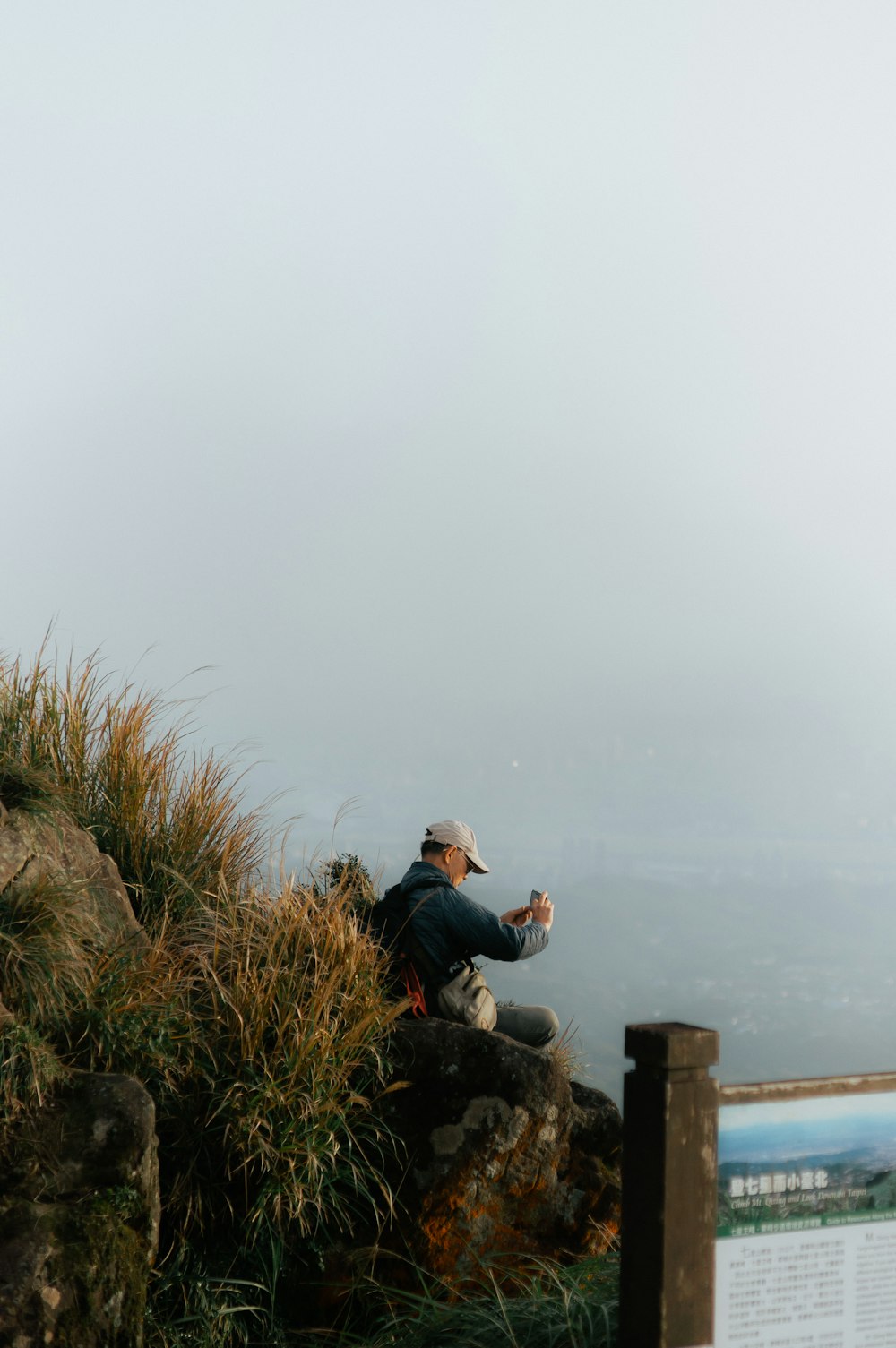 a man sitting on top of a mountain next to a sign