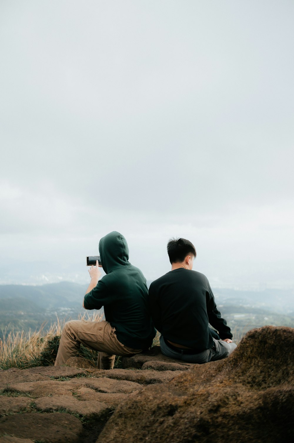 two people sitting on a rock taking a picture