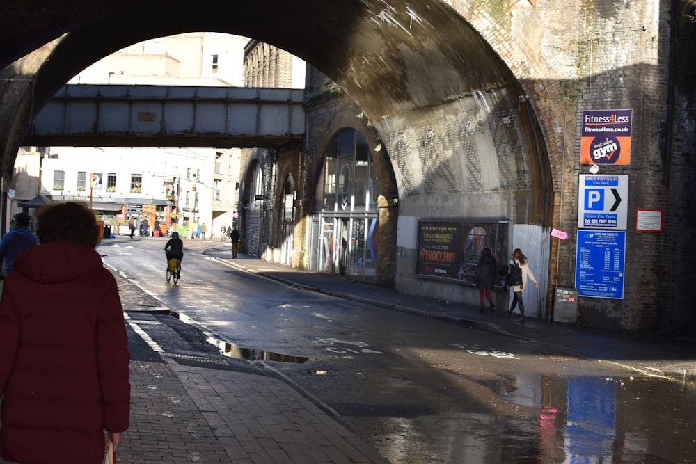 a woman in a red coat is walking under a bridge