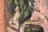 A close-up of an artwork featuring abstract forms with green and brown hues. The brush strokes create a textured surface evoking natural elements like foliage and rocks.