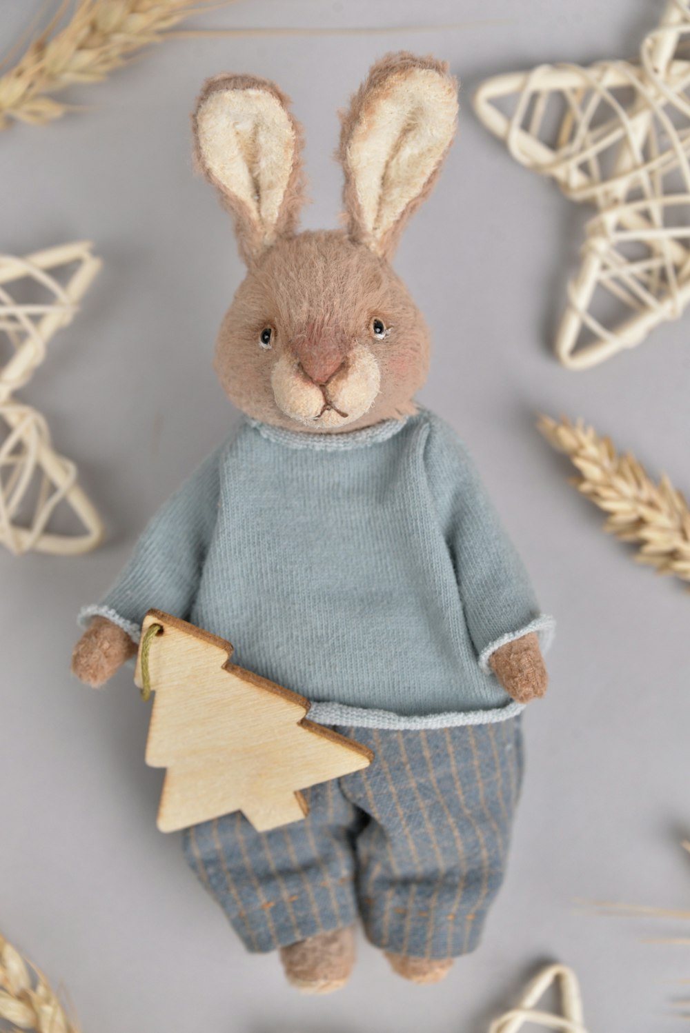 a stuffed rabbit in a sweater and pants holding a christmas tree ornament