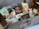 A wooden gift box filled with assorted gourmet food items including cheese, crackers, dried fruits, chocolates, and preserves. The box features brands like Bello Rustico, Marich, and Beemster. The items are attractively arranged with some packaging in clear plastic, others in paper, and the box is accented with decorative straw.