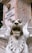 A stone sculpture of a fierce, winged lion with its mouth open, displaying its teeth prominently. The statue is weathered, with visible signs of aging and patina. Behind the sculpture, there is a stone monument with an inscription displaying text in Portuguese.