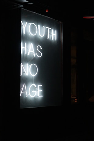 A neon sign displays the message 'YOUTH HAS NO AGE' in white glowing letters against a dark background.