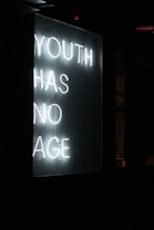 A neon sign displays the message 'YOUTH HAS NO AGE' in white glowing letters against a dark background.