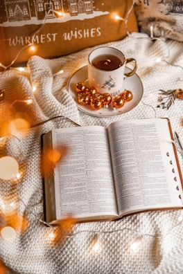 Warm neutral-toned cozy throw blanket folded beside an open book and a cup of tea.