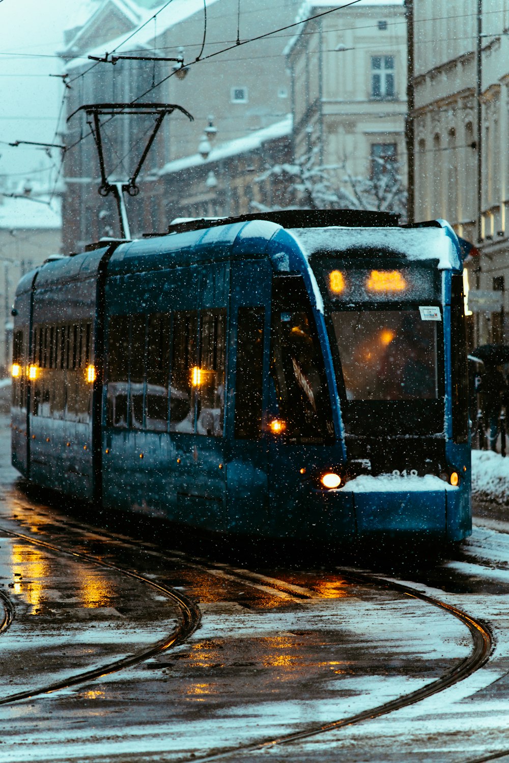 a blue train traveling down a snow covered street