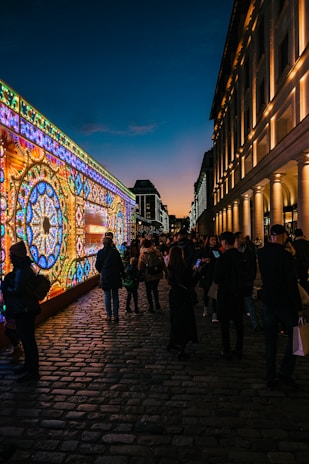 A lively street scene in Ghent with people enjoying art installations and outdoor dining at dusk.