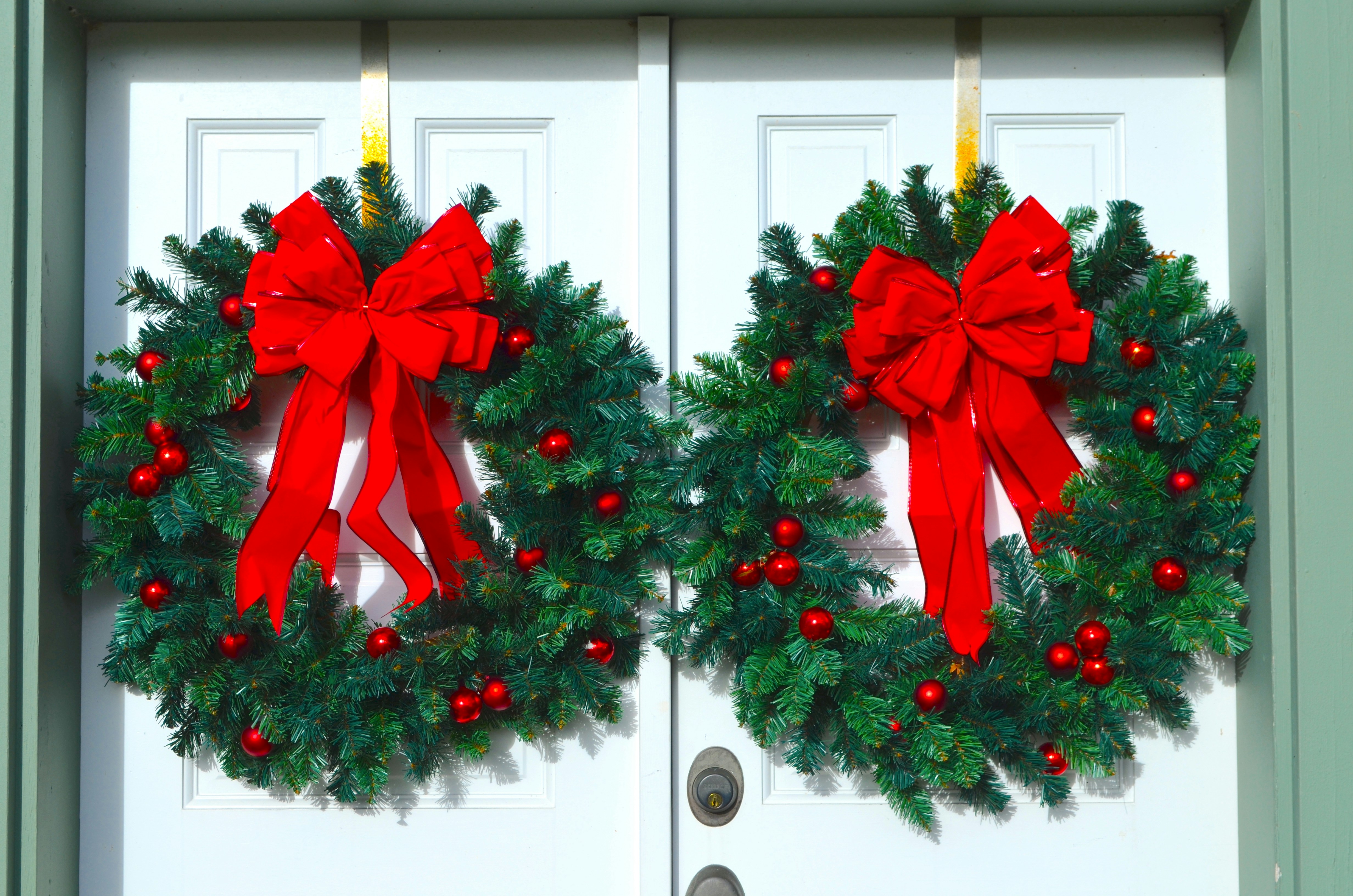 two christmas wreaths with red bows hanging on a door
