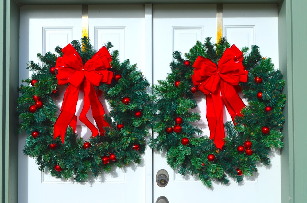 two christmas wreaths with red bows hanging on a door