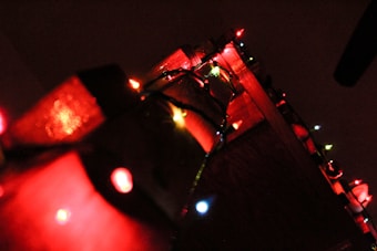 Colorful string lights are draped over a wooden surface, casting a warm and festive glow. The lights feature red and white bulbs with a few hints of green and yellow, providing a cozy ambiance.