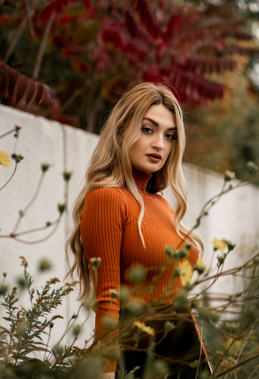 a woman in an orange sweater standing in a field of flowers