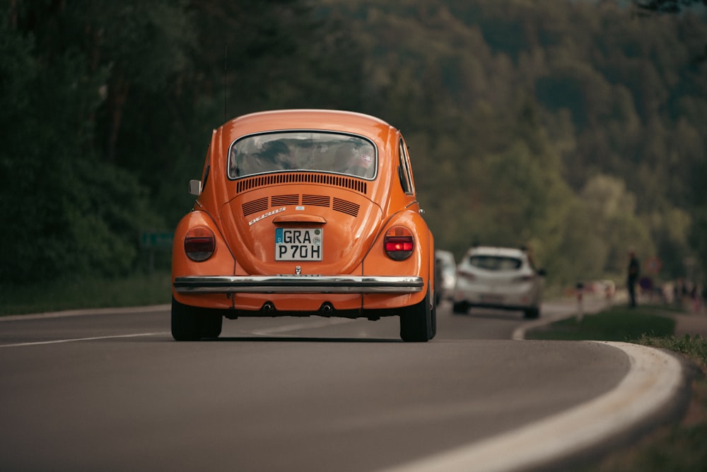 an orange car driving down a road next to a forest