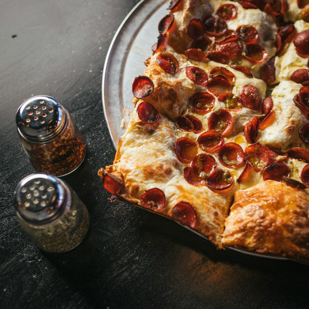 a pepperoni pizza on a plate next to a salt shaker