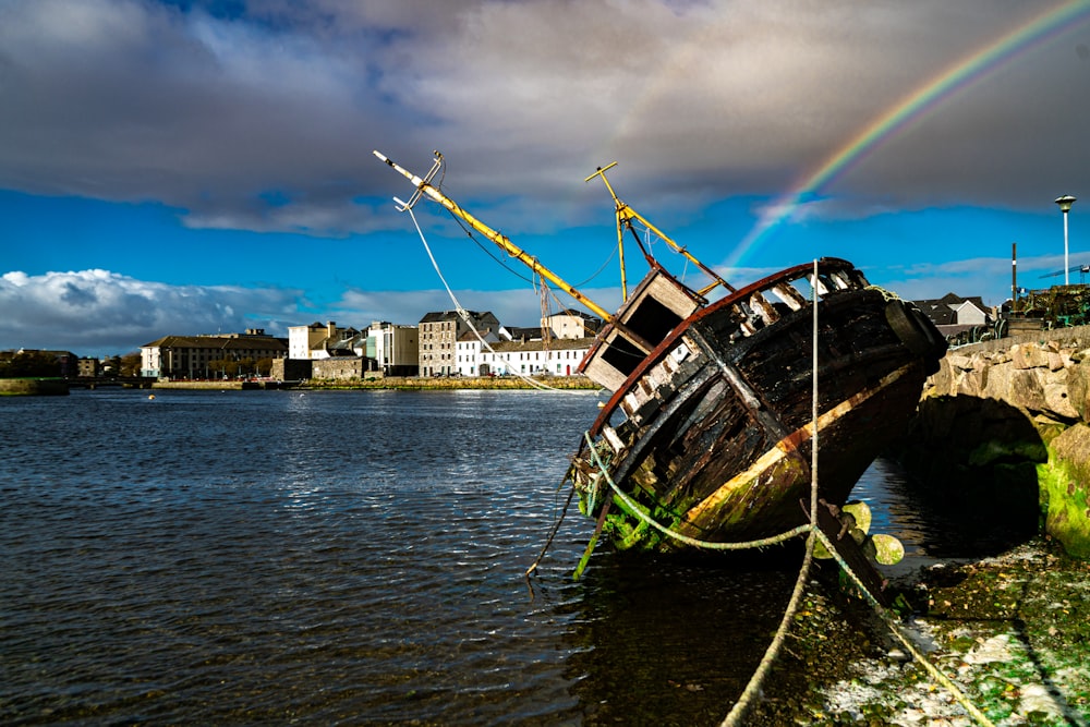 a boat sitting in the water with a rainbow in the background