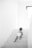 A young child in a diaper is crawling up a set of white stairs. The environment is minimalistic, with bright natural light coming from a window at the top right corner.