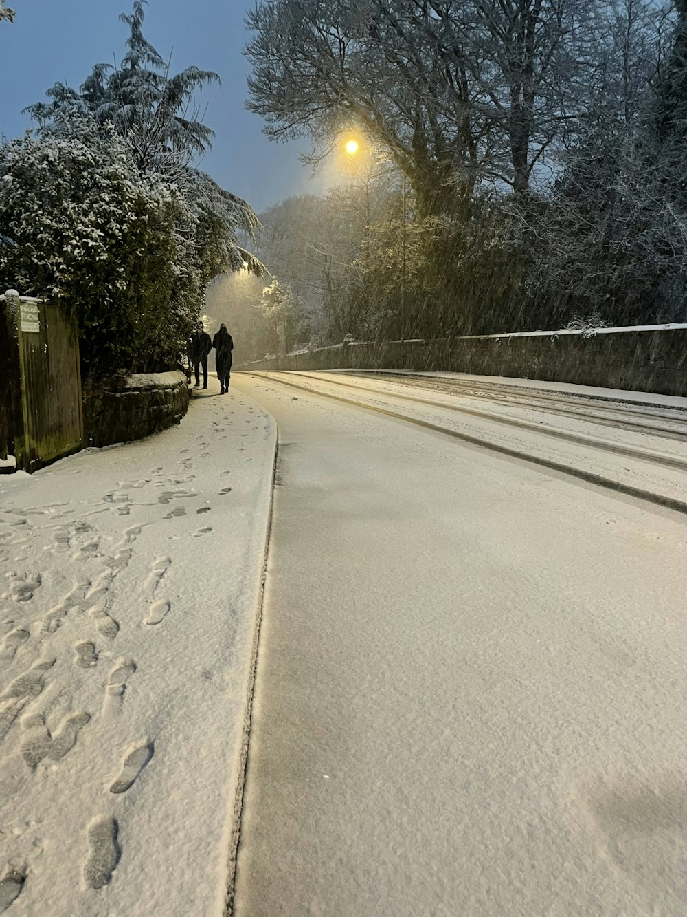 a couple of people walking down a snow covered road