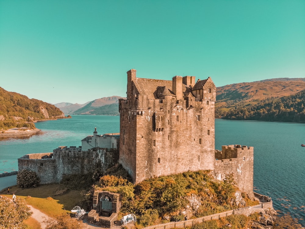 a castle sitting on top of a lush green hillside next to a lake