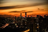 An urban skyline at sunset with glowing city lights starting to appear.