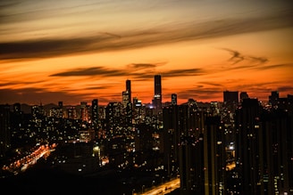 An urban skyline at sunset with glowing city lights starting to appear.