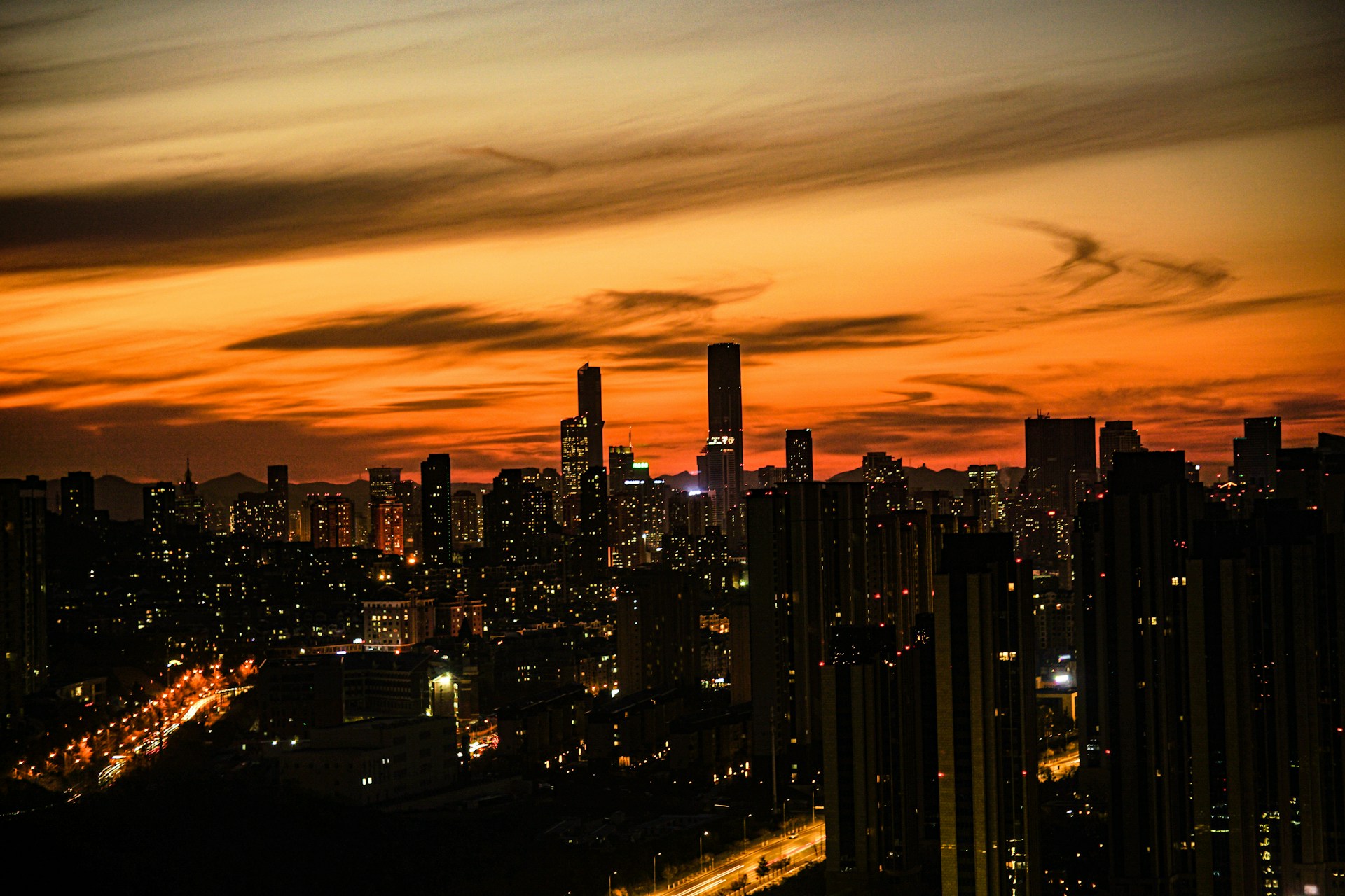 A dynamic city skyline at sunset, showcasing tall buildings illuminated by warm lights.
