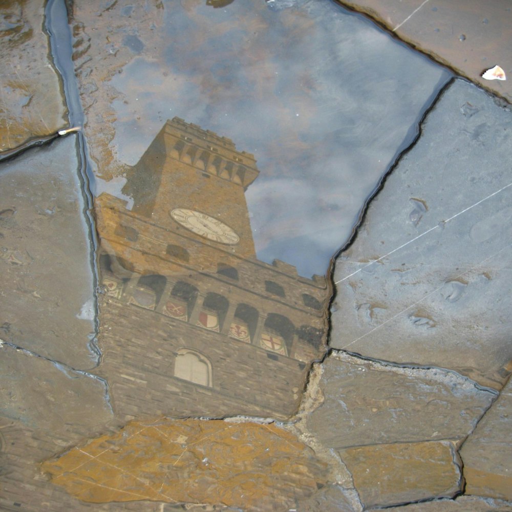 a reflection of a clock tower in a puddle of water