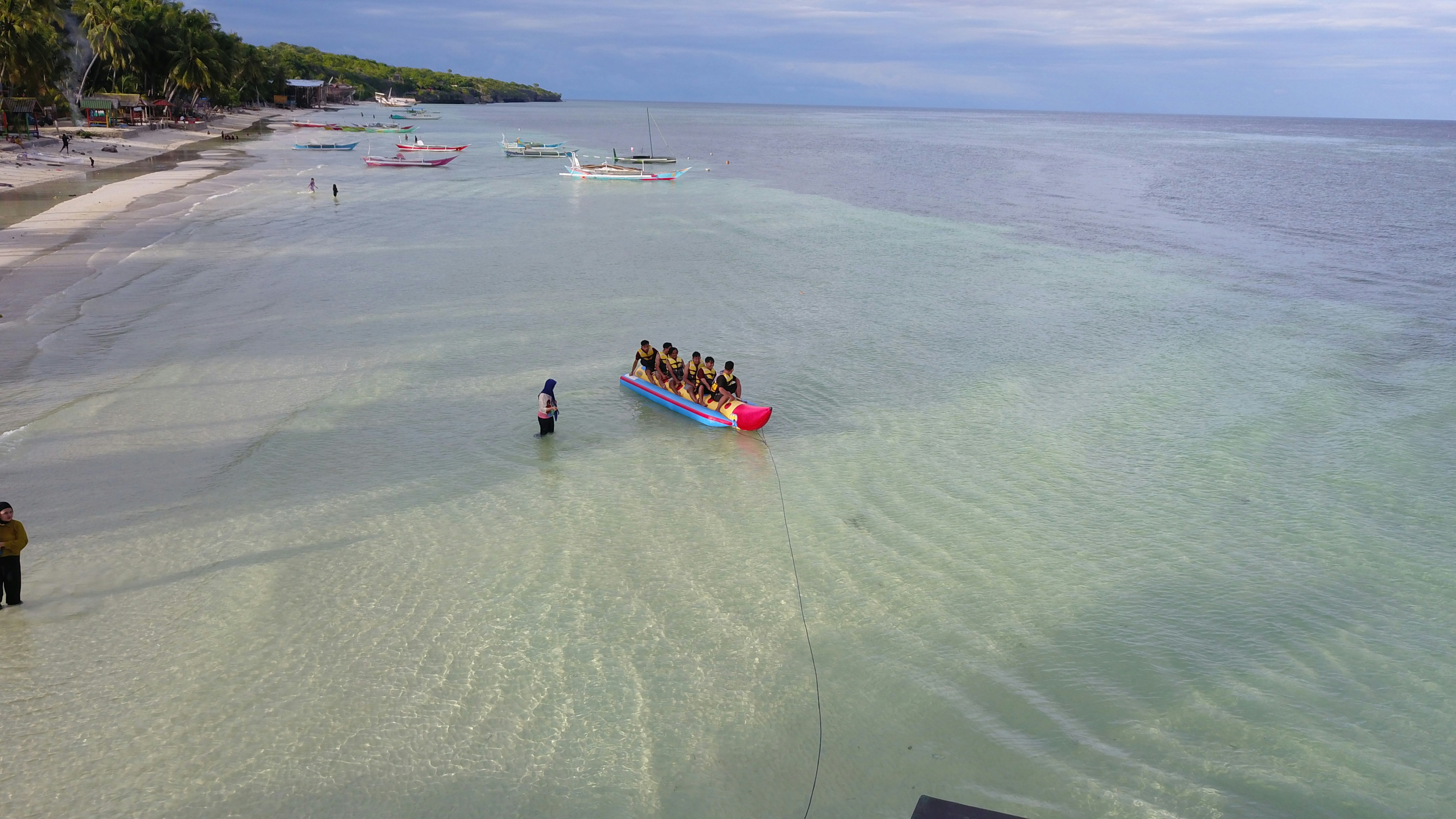 Group of people riding banana boat on calm ocean water, laughing and splashing, tropical beach
