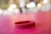 A red silicone wristband is lying on a pink textured surface. The background features soft, out-of-focus lights creating a warm ambiance.