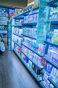 Shelves filled with a variety of skincare and personal care products inside a well-organized pharmacy or store. The shelves are stocked with creams, lotions, and other health-related items, with labels and signs displaying prices and promotions. The aisle has a clean, modern appearance with clear signage for a shopping app.