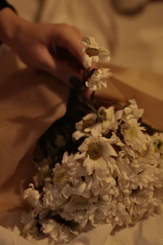 Close-up photo of a soft ivory and clay-toned bouquet wrapped in natural paper and tied with twine under warm natural light.
