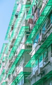 A residential building with multiple floors featuring green-tinted glass balconies and awnings. Clothes and laundry are hung out to dry on lines extending from the balconies. Air conditioning units are also visible on the walls.