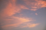 Soft, pastel-colored clouds spread across a serene sky, with hues of pink and orange blending gently into a light blue backdrop.