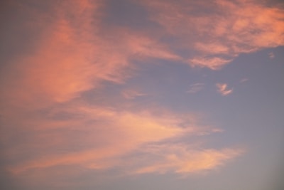 Soft, pastel-colored clouds spread across a serene sky, with hues of pink and orange blending gently into a light blue backdrop.