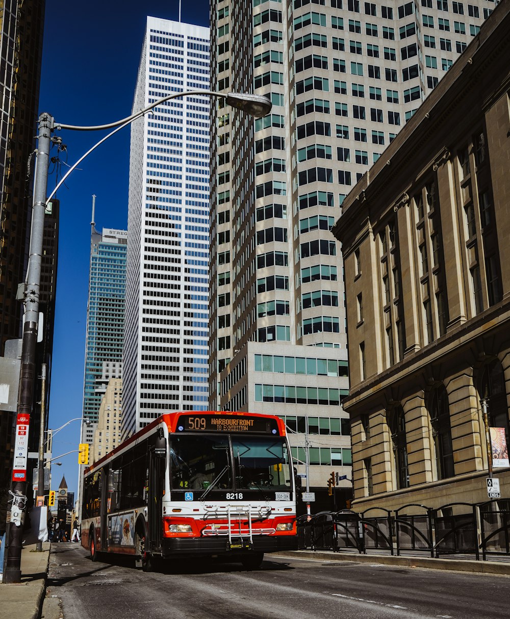 a red and white bus driving down a street next to tall buildings