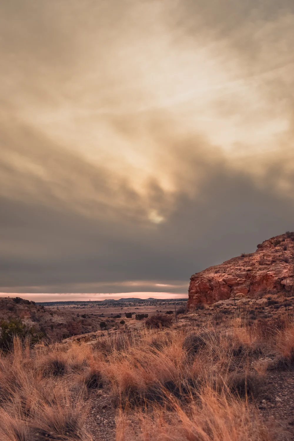 A desert mesa at dusk under a wide cloudy sky, sand and rust coloured.