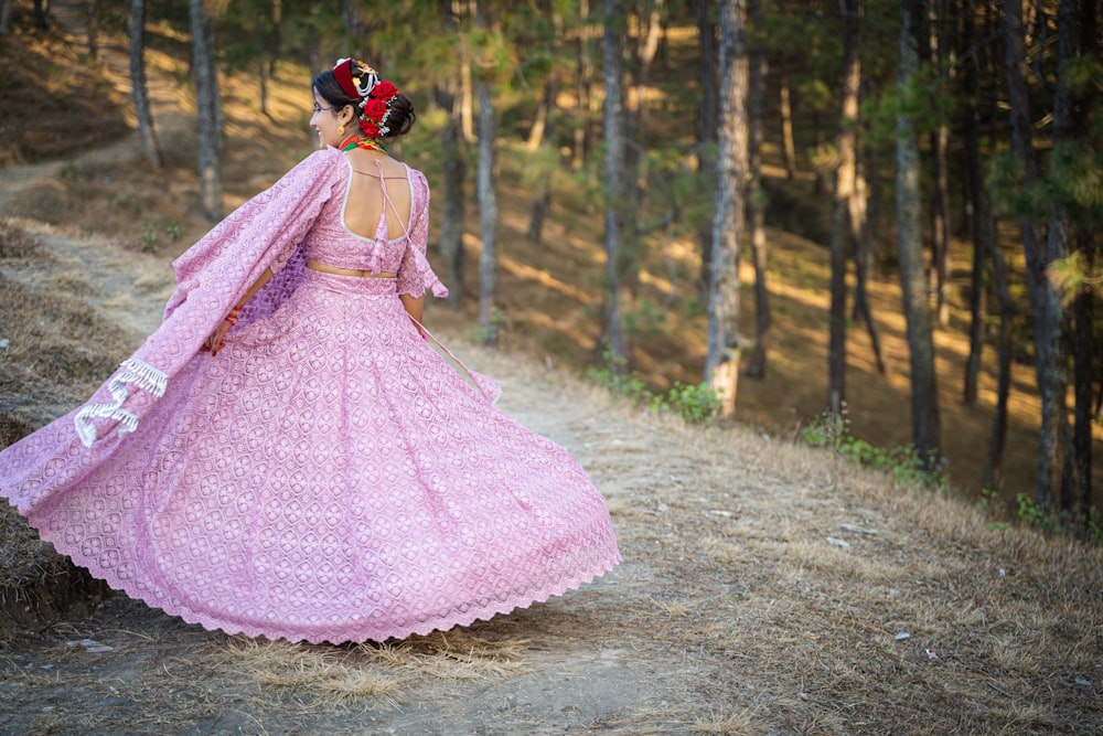 a woman in a pink dress walking down a dirt road