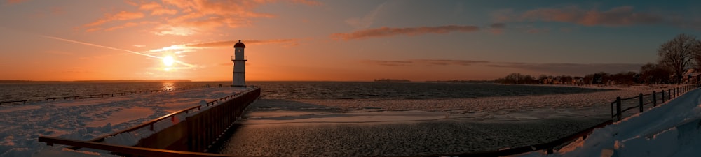 the sun is setting behind a lighthouse on a snowy day